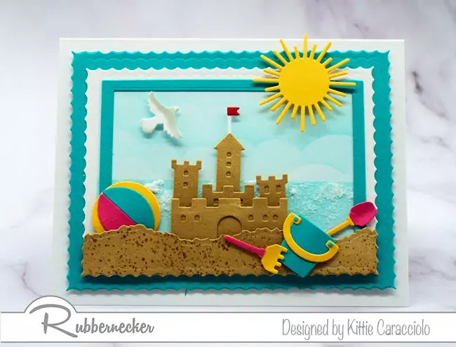 Make a sandcastle beach card with a sparkly ocean background using dies made by Rubbernecker Stamps.