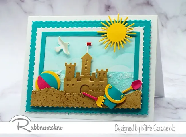 Make a sandcastle beach card with colorful beach toys and a sparkly ocean background  using dies made by Rubbernecker Stamps.