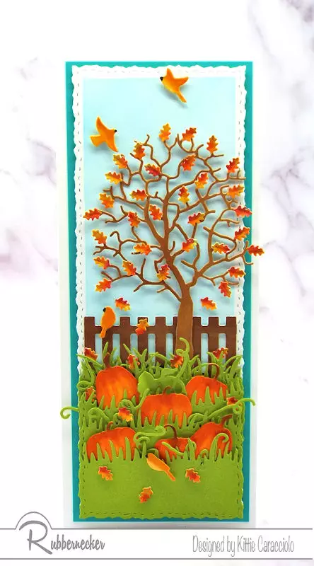 A slimline fall card showing off a die cut tree with shaped paper leaves and hand colored die cut pumpkins