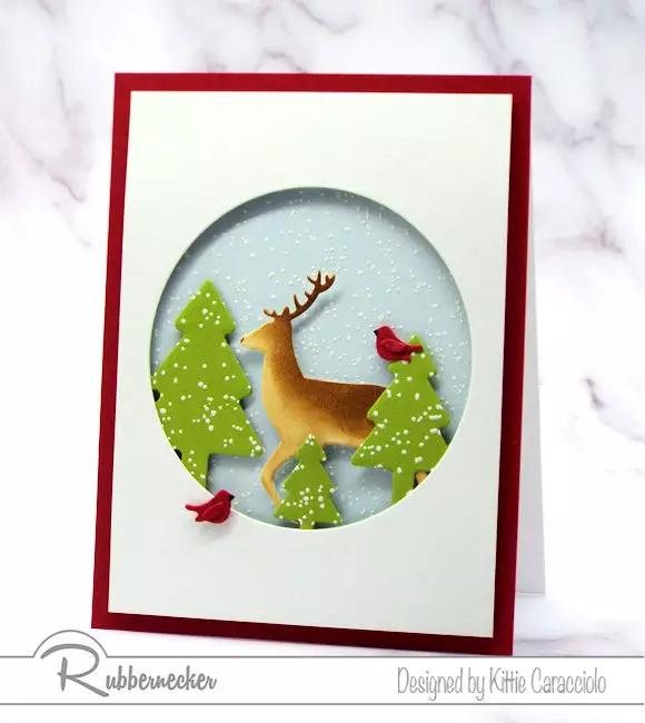 A Snowy Winter Scene on a handmade card using die cuts for the buck, cardinals, pine trees and round window from Rubbernecker
