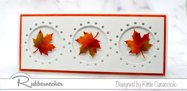One of my fall card ideas showing hand colored and die cut maple leaves centered inside three circular die cut windows on a slimline card made using all Rubbernecker products