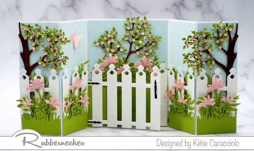 a gorgeously detailed shutter card design with a garden fence and pink flowers in different sizes all from my new dies from Rubbernecker