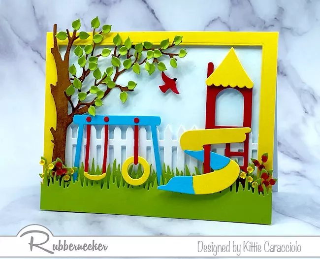 a handmade playground card with swings, a slide and lots of pretty foliage all made using new paper crafting dies from Rubbernecker