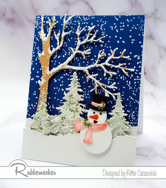 a handmade greeting card featuring embossing paste snow on the die cut branches and pine trees