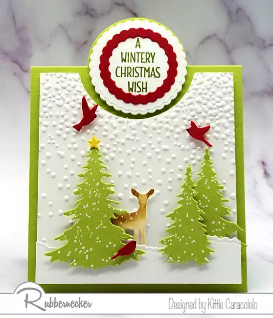 This sweet Christmas bib overlay card was made by adding die cut trees, a fawn and bold cardinals over a premade fun fold card base to create a serene winter scene.