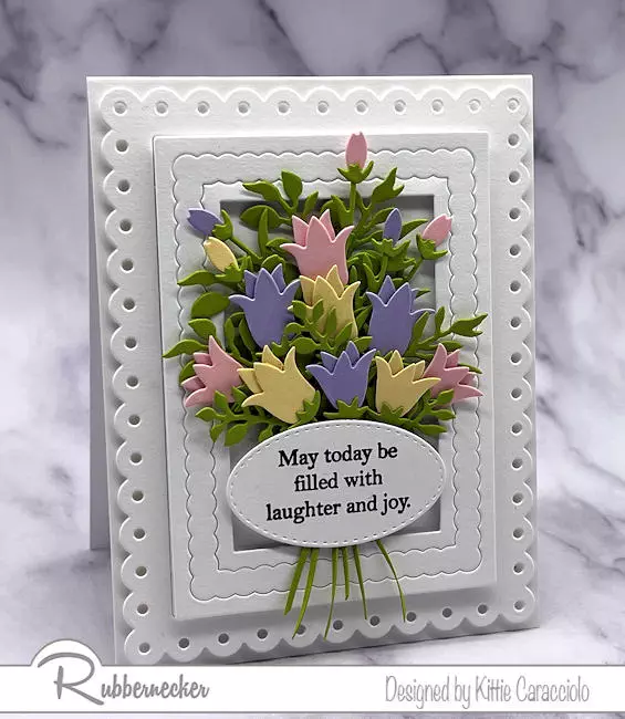 Several white on white layered frames on a handmade card add a focal point for the die cut arranged flower bouquet.