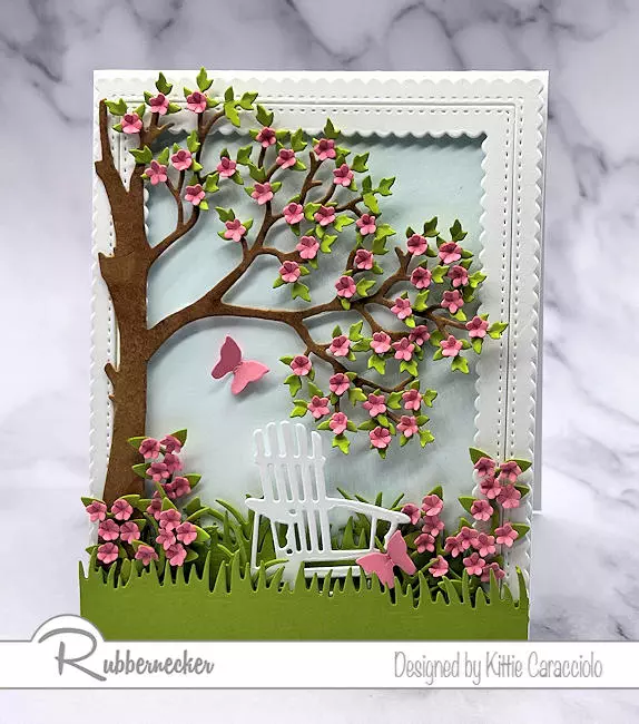 A pretty spring scene card with a beautiful flowering tree and a comfy inviting chair.