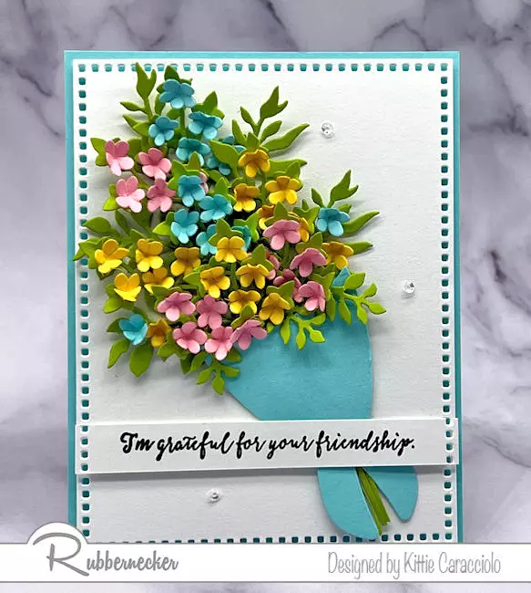 A wrapped bouquet on a handmade card loaded with lots of tiny, shaped multicolored paper flowers.