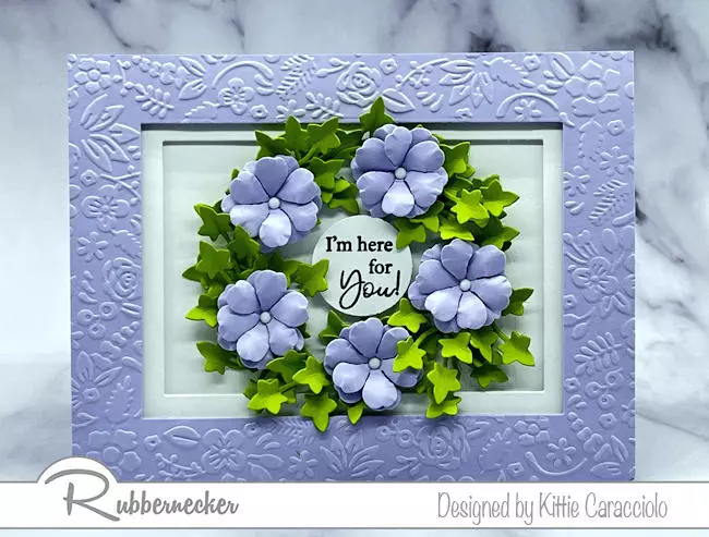 All in a beautiful shade of purple, the embossed frame and wreath of die cut paper flowers on this handmade card are very easy to make and add so much dimension.