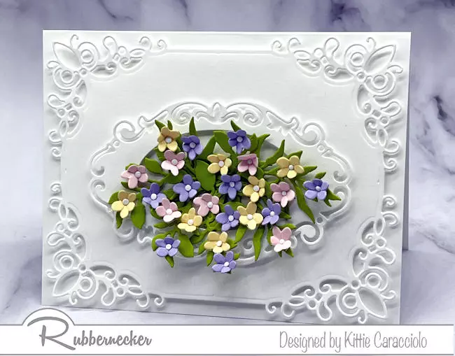 A big bunch of pastel colored tiny paper die cut flowers on a card with white on white layering to add texture and dimension.