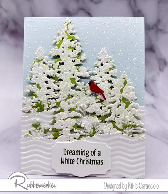 A handmade card of evergreen trees decorated with a snow effect with gesso paint for a realistic look.