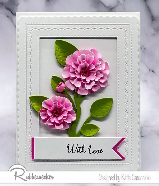 A handmade card made by inking paper flowers in shades of pink and setting them in a white on white frame.