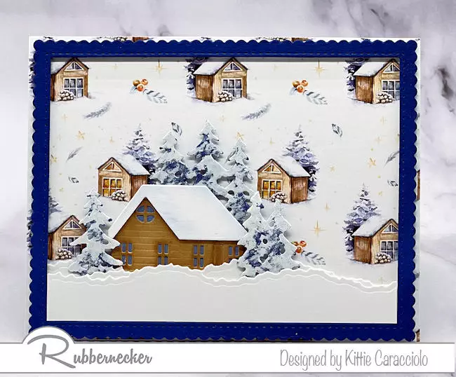 A sweet little die cut cabin sits atop a complementary patterned paper background on today