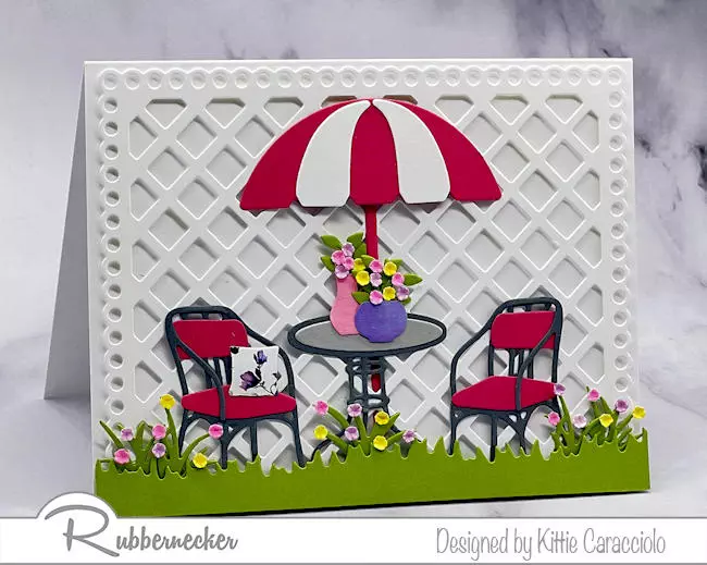 A handmade summer scene card idea with a pair of patio chairs around a table with an umbrella all made with dies from Rubbernecker.