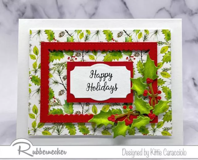 Just a few easy to make elements went into this simple handmade holly card with pops of red from the sentiment, frame and berries set over pretty patterned holly themed paper.