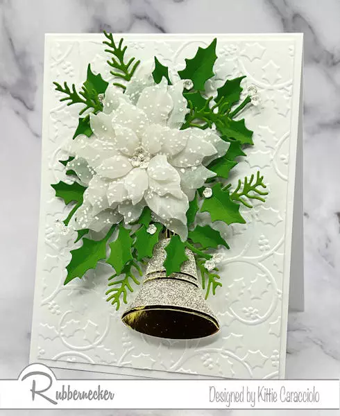 A handmade elegant white on white Christmas card with a textured poinsettia set over an embossed background with a sparkly bell for an accent.